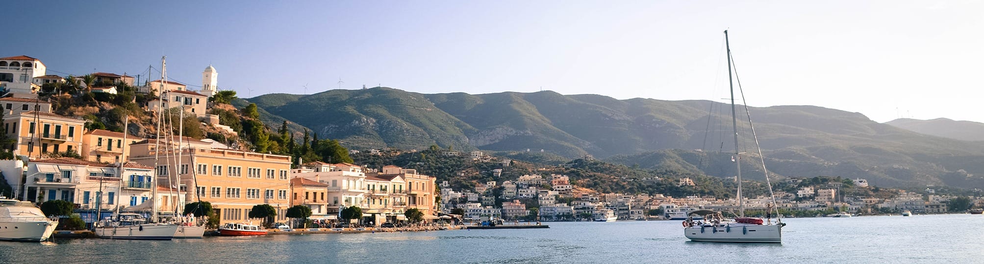 Stunning view of the Athens to Poros sailing route in Greece – A yacht gliding through the serene waters of the Saronic Gulf, framed by lush green hills and charming coastal villages.