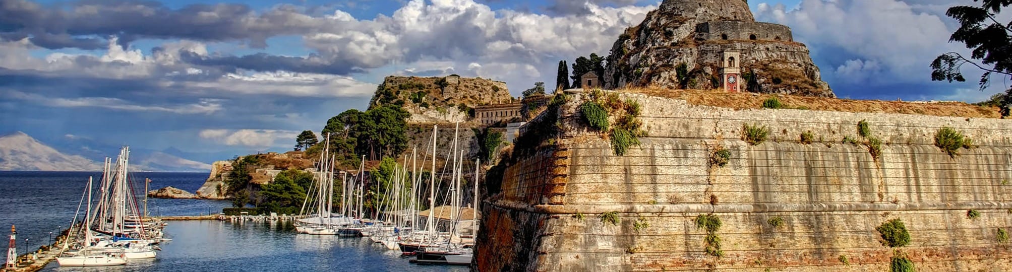 Charming view of the Corfu sailing route with Corfu Town in the background – A yacht sailing through the clear blue waters of the Ionian Sea, showcasing the historic architecture and lush landscapes of Corfu.
