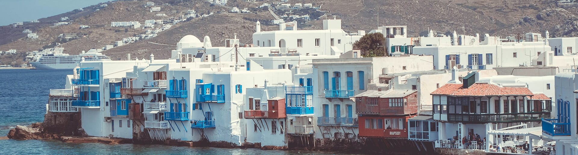 Vibrant view of the Cyclades sailing route to Mykonos, Greece – Yacht navigating the picturesque Aegean Sea, surrounded by the iconic white-washed buildings and lively coastal scenery of Mykonos.