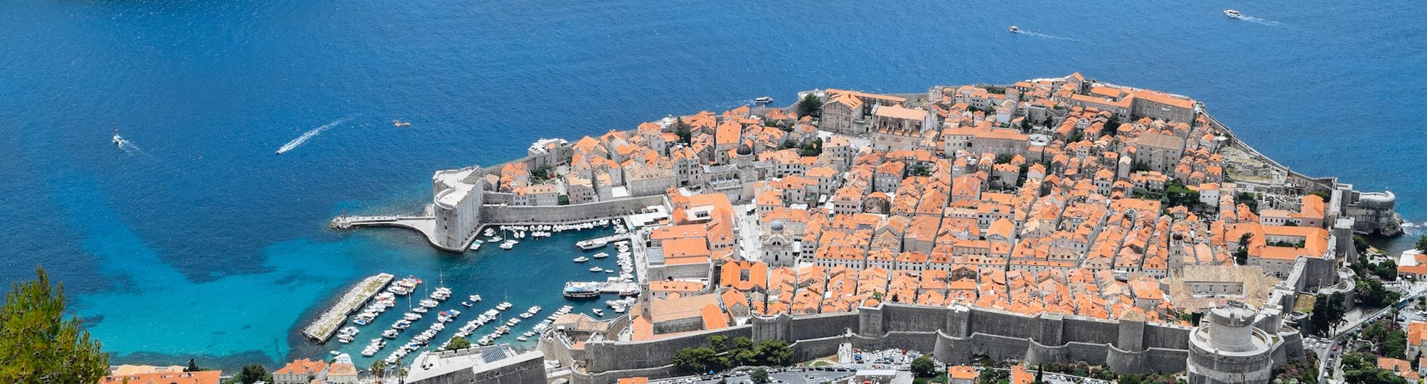 Captivating view of the Dubrovnik sailing route in Croatia – A yacht cruising the azure waters of the Adriatic Sea, with the historic city of Dubrovnik and its iconic city walls and red-roofed buildings set against a dramatic coastal backdrop.