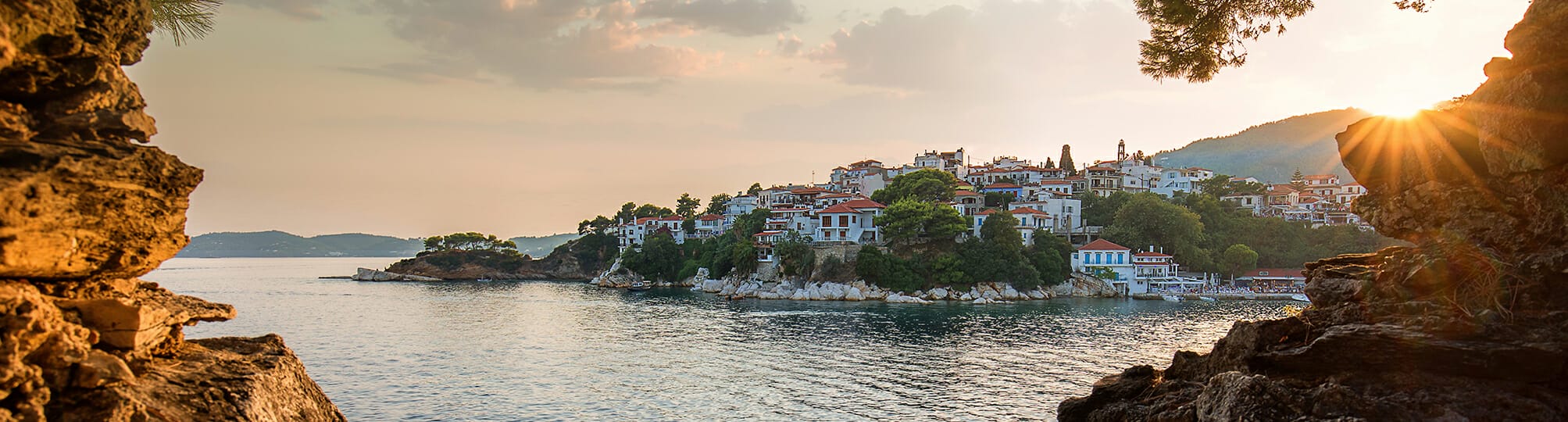 Breathtaking sunset view along the Sporades sailing route near Skiathos, Greece – A yacht sailing on the calm waters of the Aegean Sea, with vibrant hues of orange and pink illuminating the sky and reflecting on the water.