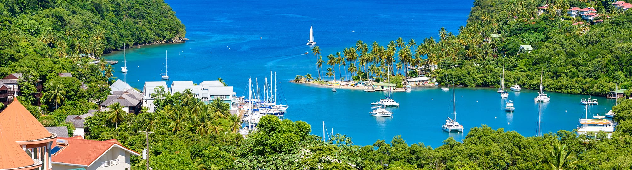 Beautiful view of Marigot Bay, St. Lucia, in a sailing itinerary – A yacht anchored in the serene waters, framed by lush hills and vibrant tropical vegetation, highlighting the picturesque scenery of this Caribbean sailing destination.