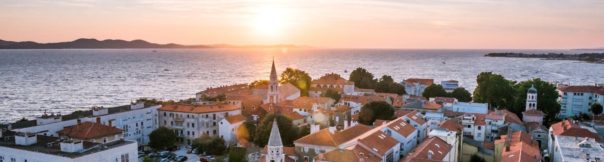 Scenic view of the Zadar sailing itinerary in Croatia – A yacht gliding through the tranquil waters of the Adriatic Sea, with the historic city of Zadar and its beautiful coastline visible in the background, showcasing stunning sunsets and ancient architecture.
